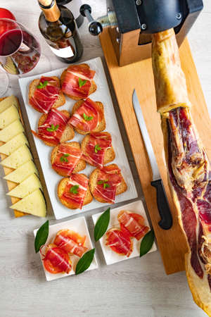Tapas and appetizers of Iberian ham with a glass of wine, ripe tomatoes and cow cheese on a white wooden background.の写真素材
