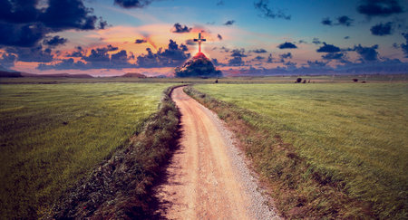 Landscape of crop fields and grassy meadows at sunset and road or path to the mountain with cross on top.の写真素材