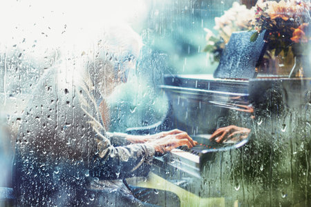 Playing piano song behind the window with water drops on a rainy day. Sad music for travel road.の写真素材