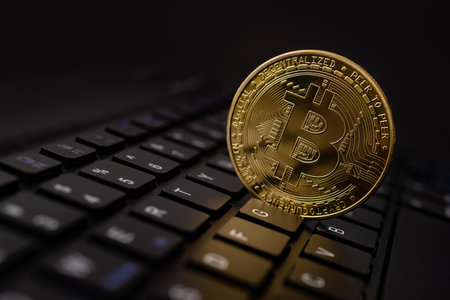 Bitcoin gold coins on futuristic and abstract background over black laptop keyboard. Finance and...