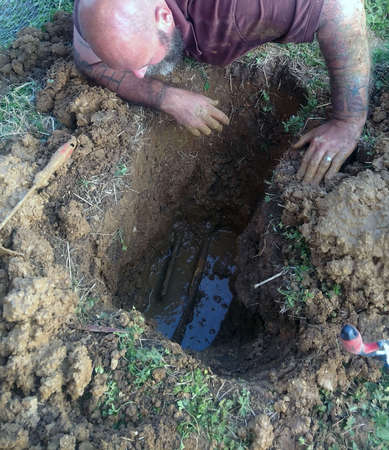 Man peering into water filled trench at broken pipesの写真素材