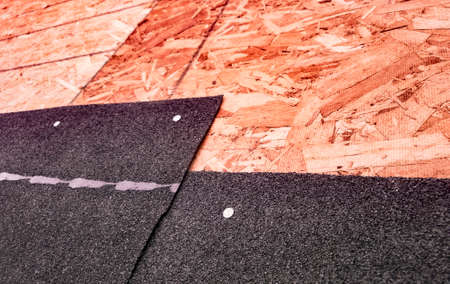 Closeup of overlapping black asphalt shingles and underlying oriented strand board subroof materialの写真素材