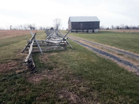 White oak split rail fence alongside dirt road leading to barn in distanceの写真素材