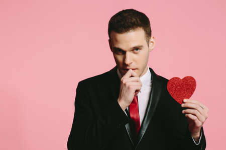 Handsome man in a black suit holding a red heart for Valentine's Dayの写真素材