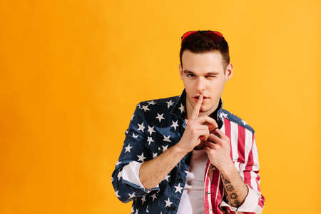 Cute guy with finger on mouth and one eye winking in american flag jackeの写真素材