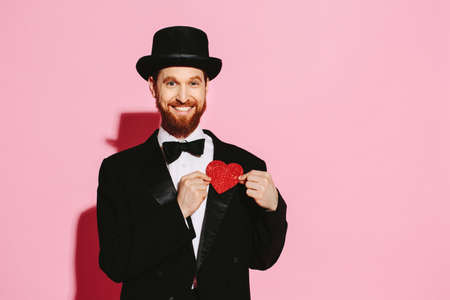 Smiling man in a tuxedo and top hat holding a red heartの写真素材