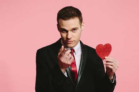 Handsome man in a black suit holding a red heart for Valentine's Dayの写真素材