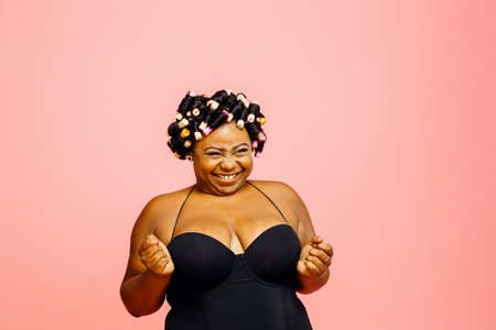 Woman with hair curlers and neglige grinning and looking to side, isolated on pink backgroundの写真素材