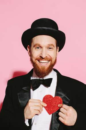 Happy man in a tuxedo and top hat holding a red heartの写真素材