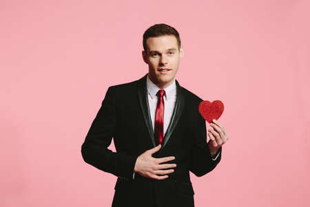 Handsome man in a black suit holding a red heart for Valentine's Dayの写真素材