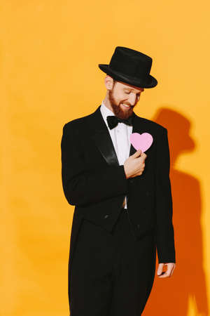 Hopeful smiling man with top hat holding a pink heart, be my valentineの写真素材