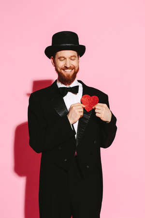 Smiling man in a tuxedo and top hat holding a red heartの写真素材