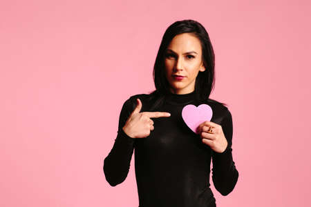 Woman in black pointing at pink heart in her handの写真素材