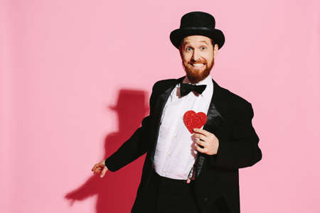 Smiling and dancing man in a tuxedo and top hat holding a red heartの写真素材