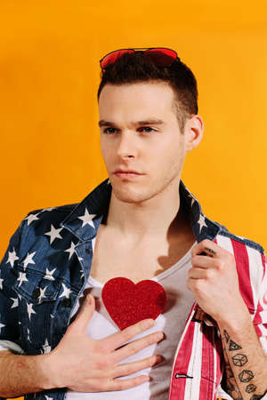 All-American handsome guy holding red heart on chest in american flag jacketの写真素材