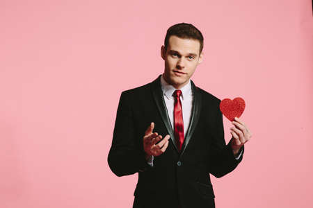 Handsome man in a black suit holding a red heart for Valentine's Dayの写真素材