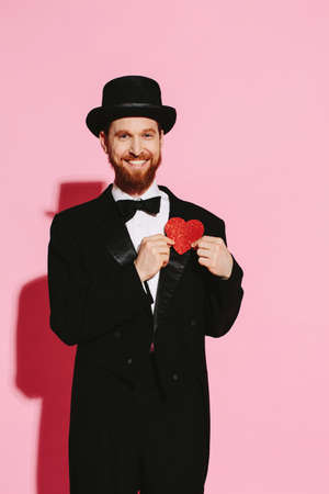 Smiling man in a tuxedo and top hat holding a red heartの写真素材
