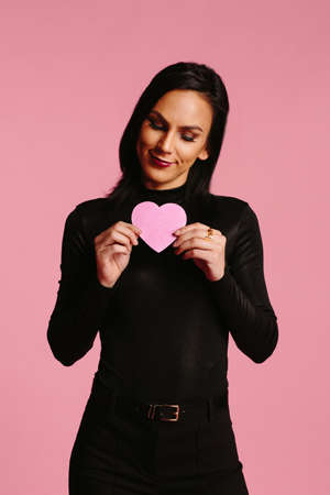 Woman in black looking down and holding a pink heartの写真素材