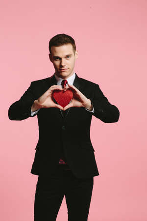 Handsome man in a black suit holding a red heart for Valentine's Dayの写真素材