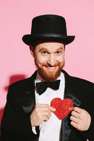 Smiling man in a tuxedo and top hat holding a red heartの写真素材