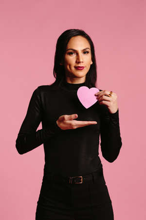 Woman in black displaying pink heart in her handの写真素材