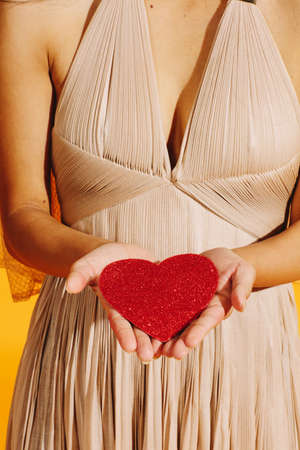 female hands holding a red heart in beige pleated dressの写真素材