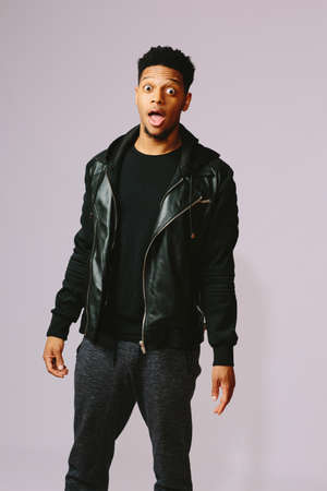 Shocked young African American man with open mouth wearing a black jacketの写真素材