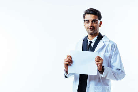 Portrait of a man in business suit, lab coat and protective glasses, looking at camera, holding a...