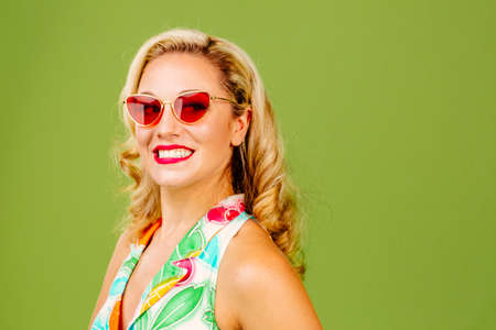 Beautiful blonde with big smile and sunglasses, isolated on green studio background