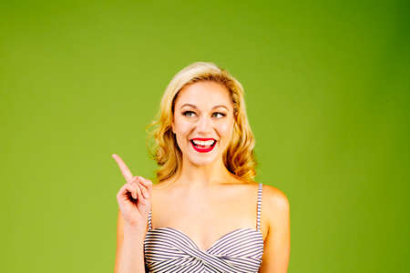 Look at this, portrait of a beautiful blonde woman in striped bikini pointing and looking to side,...