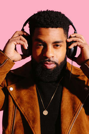 Close up portrait of a cool man with beard holding headphones isolated on pink studio backgroundの写真素材
