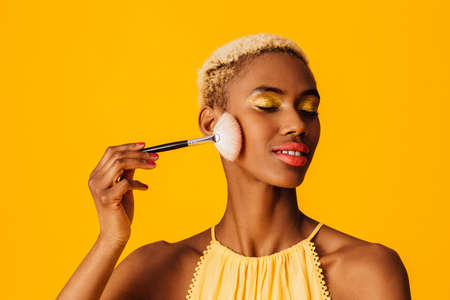 Portrait of a beautiful young woman applying cover up loose powder  to her cheeks with a makeup...