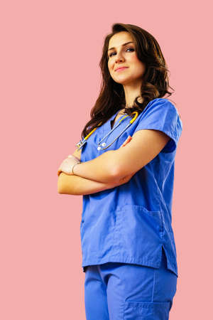Portrait of smiling female doctor or nurse in blue uniform with arms crossed on pink studio backgroundの写真素材