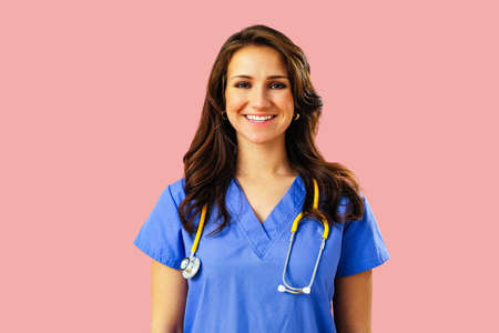 Portrait of smiling female doctor or nurse with stethoscope in blue uniform on pink studio backgroundの写真素材