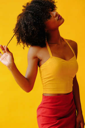 portrait of beautiful young African american woman in bright summer outfit posing isolated on yellow backgroundの写真素材