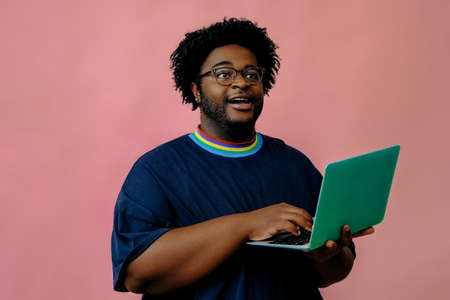 young african american man posing with laptop in the studio over pink backgroundの写真素材