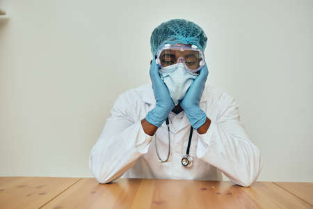 Male Doctor Wearing Protection Sitting At Deskの写真素材