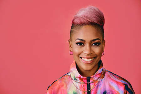 Portrait of a happy stylish young woman with pink hair and colorful fashion jacket on pink backgroundの写真素材