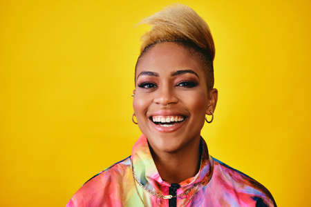 Happy Stylish young woman smiling with cool trendy short hair, jewelry and colorful jacket Against...
