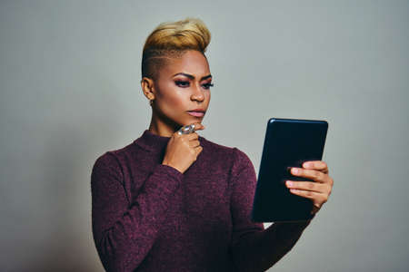 Young woman thinking while Using Tablet device Against Gray Background