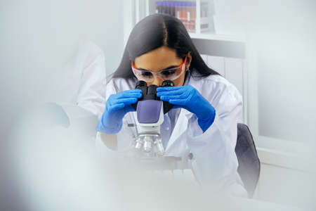 Beautiful young scientist or laboratory assistant using microscope in labの写真素材