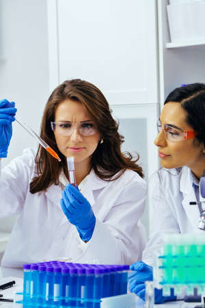 Two beautiful young female scientists working in laboratory with test tubes doing some research