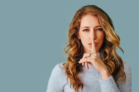portrait of a beautiful young woman with long curly hair wearing sweater finger on lips secret hush