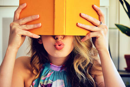 young college woman covering eyes with yellow bookの写真素材