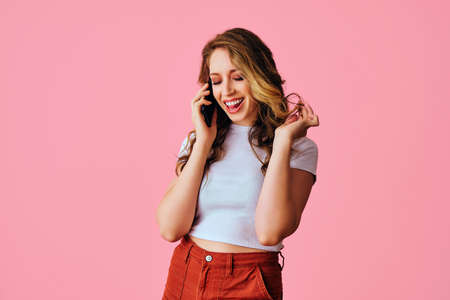 portrait of beautiful young adult woman with curly hairstyle and white shirt talking on mobile phone...