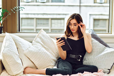thoughtful beautiful young adult woman with tablet pc on sofa at homeの写真素材
