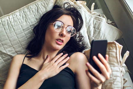 young adult woman inspired using mobile phone while lying in bed