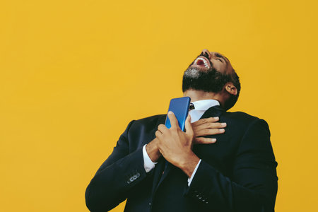portrait of smiling positive handsome bearded man in suit and tie with smartphone video call hand on heart yellow backgroundの写真素材