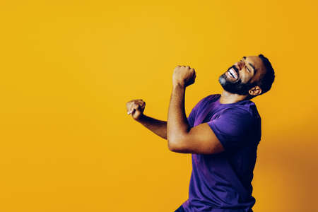 portrait of a successful winner man with a beard and a purple t-shirt celebrating dancing with arm...