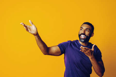 young black man with beard and mustache smiling and looking away at copy space hand signal isolated blue backgroundの写真素材